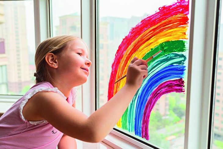 Mädchen malt in der häuslichen Quarantäne einen Regenbogen ans Fenster - ein Zeichen der Hoffnung